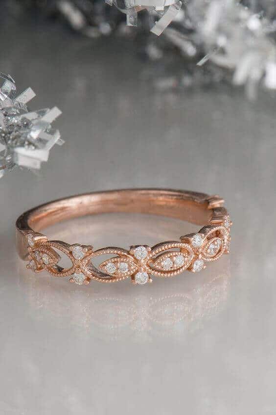 Vintage rose gold diamond wedding band featuring marquise links and milgrain detail, resting on a reflective surface with silver bokeh background.
