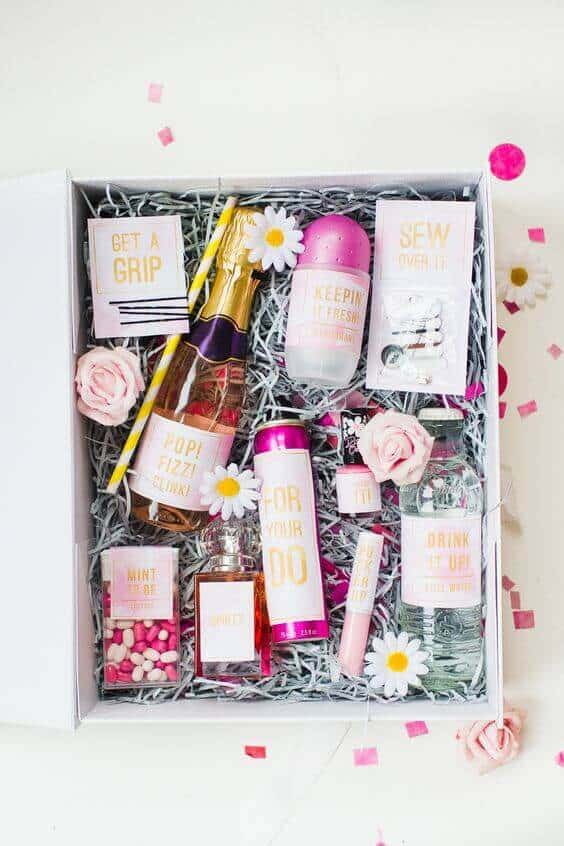 20 clever bridal shower gift ideas to be innovative 7 Top-down view of a blush-and-gold bridal shower gift box filled with wedding essentials, including mini champagne, deodorant, and faux flowers.