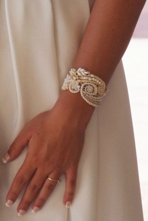 38 wedding accessories list - ideas to transform your big day into magic 7 Close-up of a pearl-embellished gold cuff on a bride's wrist, contrasting against her ivory wedding dress, highlighted by soft, diffused lighting.
