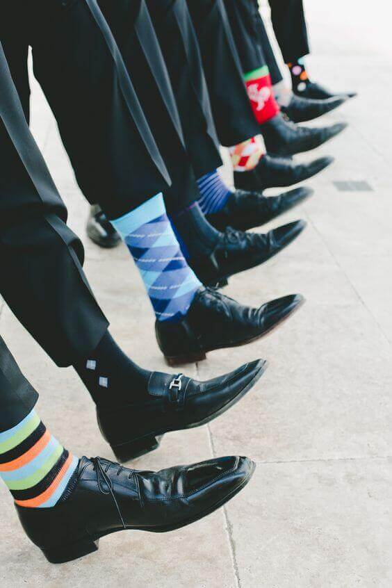 38 wedding accessories list - ideas to transform your big day into magic 8 Groomsmen showcase bold, mismatched socks under tailored black trousers on a sunlit terrace, adding playful flair to wedding accessories.