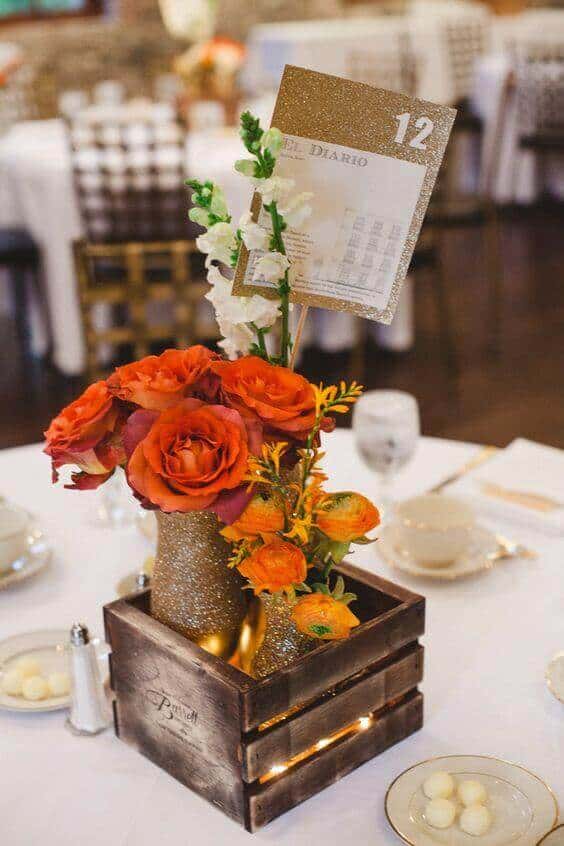 31 autumn wedding flowers ensembles perfect for your special day 9 Rustic-glam wedding table centerpiece featuring orange roses, ranunculus, and fairy lights in gold-glitter vases, set with white dinnerware.