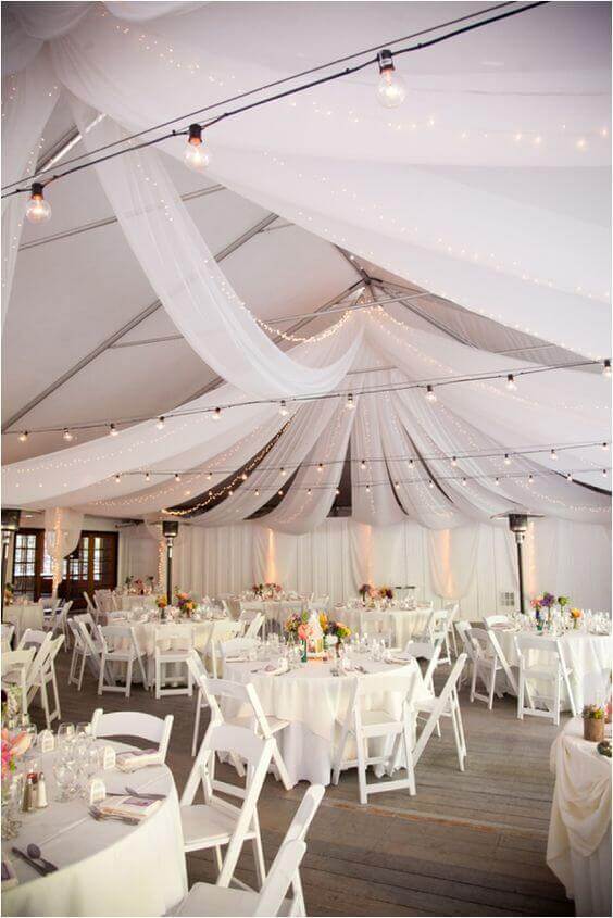 37 Morning Wedding Ideas filled with Sunshine color pallets 15 Tented wedding reception featuring white draping, twinkle lights, round tables with floral centerpieces, and a romantic ambiance.