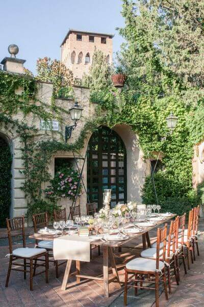 37 Morning Wedding Ideas filled with Sunshine color pallets 16 Sun-dappled outdoor banquet table set for a romantic morning wedding, adorned with blush florals, candles, and ivy in a Tuscan courtyard.