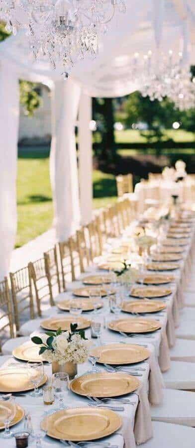 37 Morning Wedding Ideas filled with Sunshine color pallets 18 Elegant outdoor morning wedding reception featuring a long banquet table adorned with gold chargers, crystal chandeliers, and lush white florals.