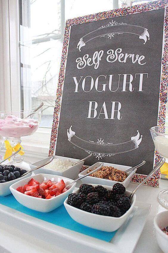37 Morning Wedding Ideas filled with Sunshine color pallets 24 Chic self-serve yogurt bar for a wedding brunch, featuring a chalkboard sign, white bowls of berries, granola, and yogurt, set on a blue mat.