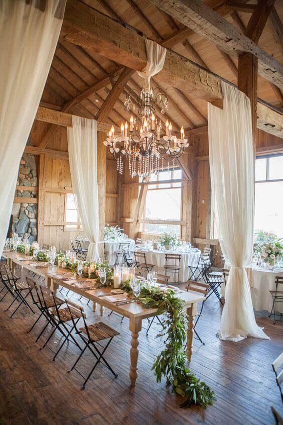 Rustic-chic barn reception with a crystal chandelier, candlelit tables, and lush greenery, perfect for timeless wedding theme ideas.