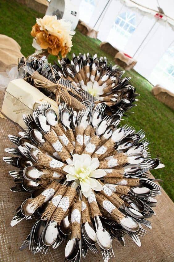 Rustic flatware station under a wedding tent, featuring burlap and lace-wrapped cutlery arranged in sunburst patterns on round trays.