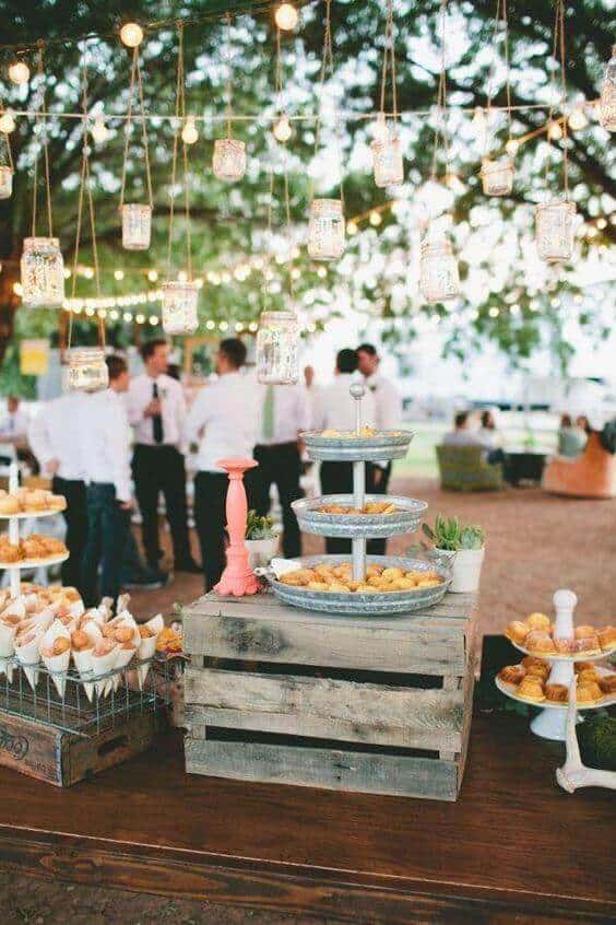 37 Morning Wedding Ideas filled with Sunshine color pallets 31 Rustic outdoor morning wedding dessert table under twinkling lights, featuring golden pastries, guests mingling, and a cozy atmosphere.