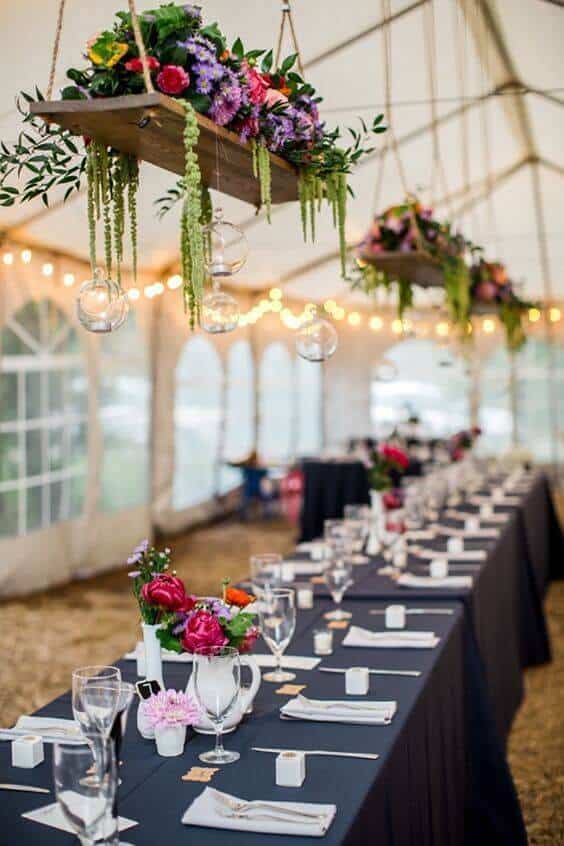 Rustic-elegant wedding setup in a marquee tent, featuring suspended florals, candlelit tables, and warm bistro lights for an intimate atmosphere.