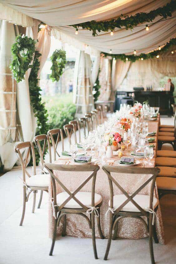 37 Morning Wedding Ideas filled with Sunshine color pallets 34 Long banquet table under a tent, adorned with a blush sequined tablecloth, greenery garlands, and pastel floral centerpieces.