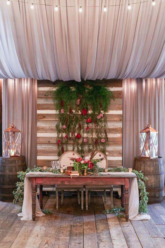 Rustic-luxe sweetheart table in a barn, adorned with a blush-champagne runner, lush florals, and glowing lanterns, perfect for intimate receptions.