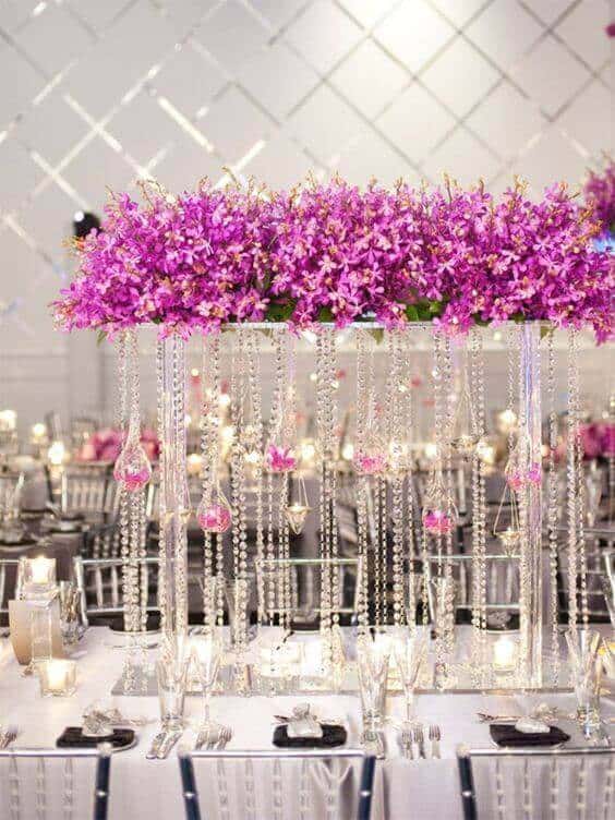 Glamorous wedding theme featuring an elevated fuchsia orchid centerpiece with cascading crystal strands, set on a mirrored table in a candlelit ballroom.