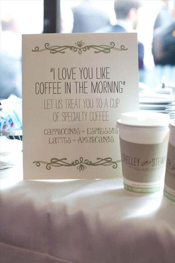 37 Morning Wedding Ideas filled with Sunshine color pallets 9 A cozy wedding coffee bar with a backlit sign reading a romantic quote. Compostable cups rest on a white linen table, inviting guests for specialty coffee.