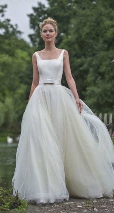34 fancy wedding dresses and designs to make your big day sparkle 28 Full-length bridal portrait of a bride in a fancy wedding dress featuring a satin bodice and layered tulle skirt, set in a serene garden by a pond.