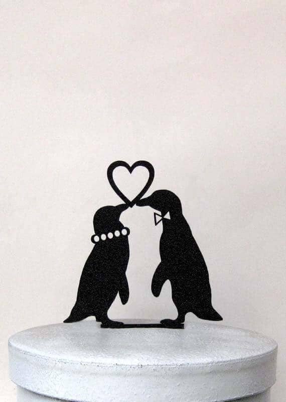 Minimalist black penguin couple cake topper forming a heart with their beaks on a smooth pale wedding cake.