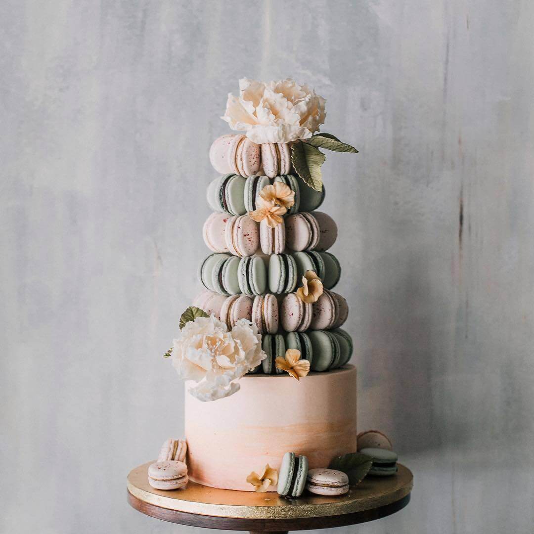 Pastel macaron tower wedding cake on a gold pedestal, topped with sugar peonies and arranged in concentric tiers.