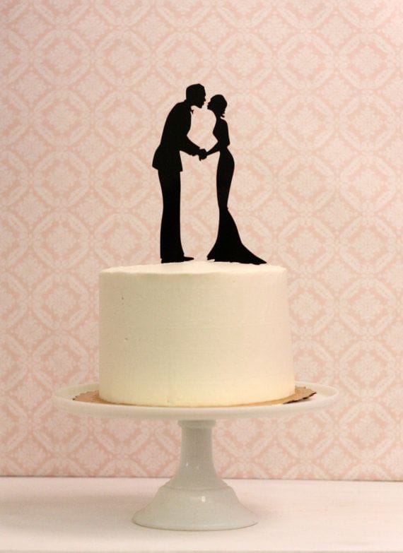Minimalist wedding cake featuring a smooth ivory buttercream finish, topped with a sleek black silhouette of a couple kissing.