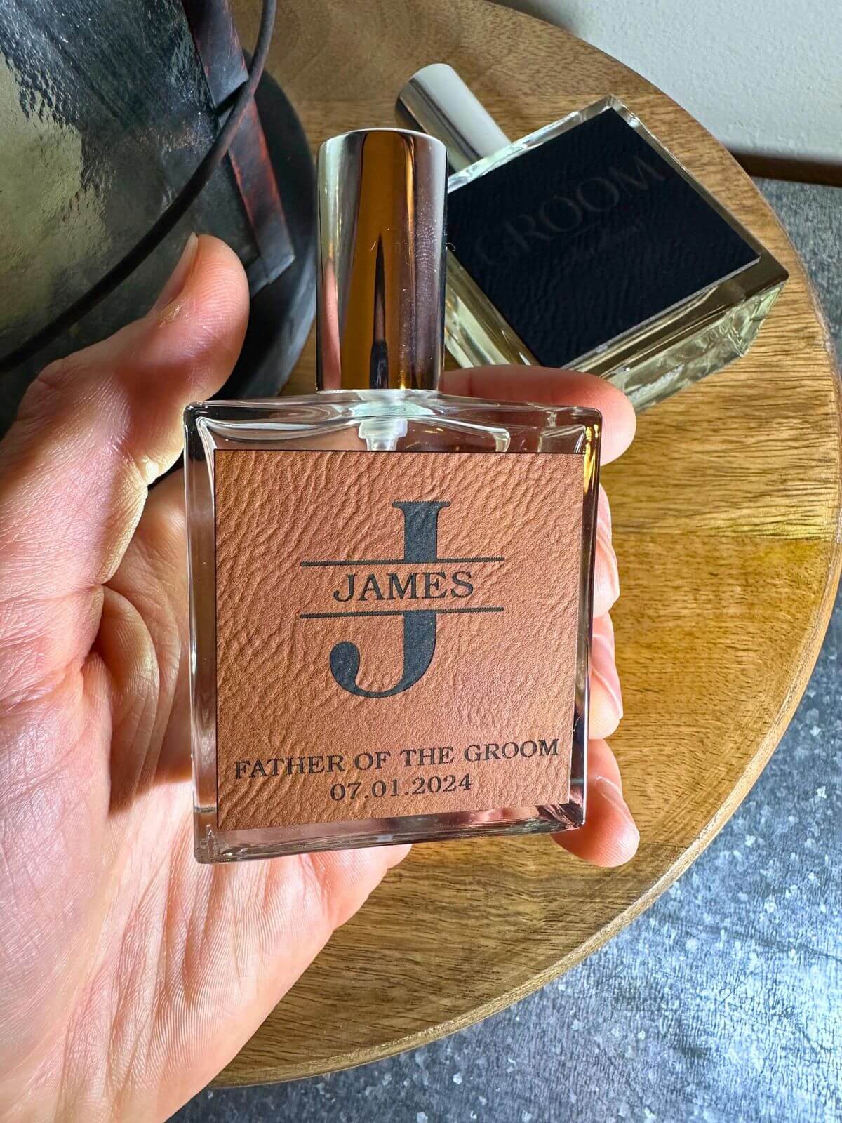 Personalized cologne bottle with monogram and date for the Father of the Groom, showcased on a wooden tray, perfect for groomsmen gift ideas.