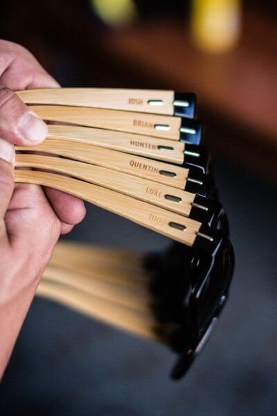 Close-up of six pairs of personalized bamboo sunglasses with engraved names, fanned out in warm, rustic lighting, ideal groomsmen gifts.